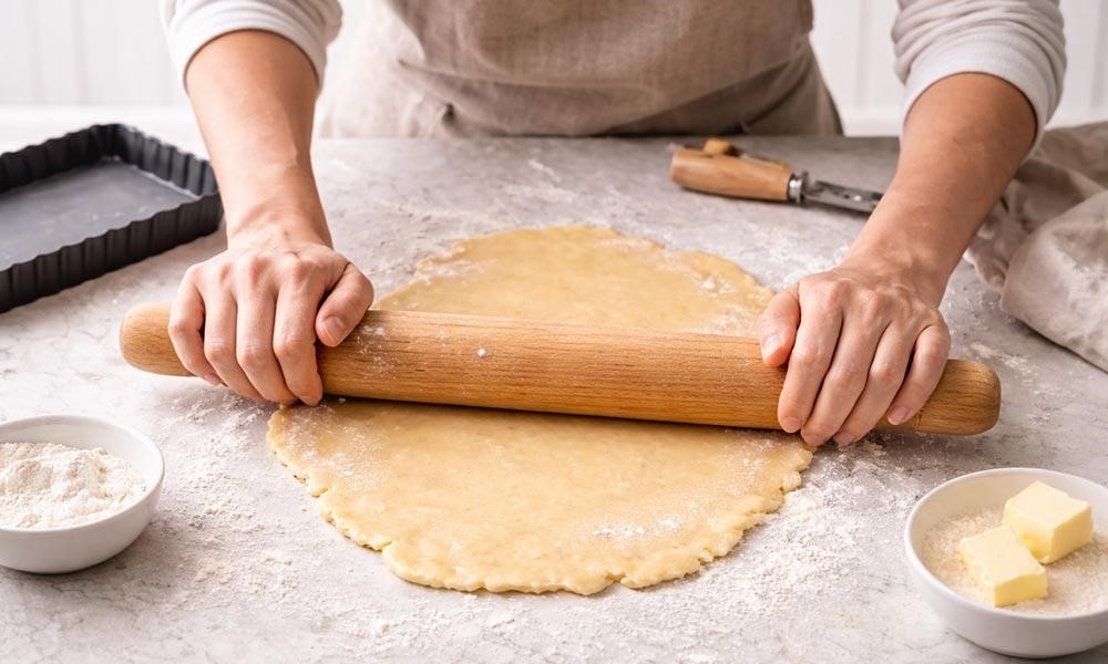 شخصی در حال پهن کردن خمیر تارت روی میز
